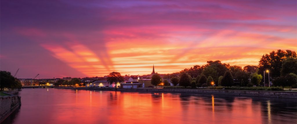 Downtown Janesville skyline and Rock River under a vivid pink sunset.