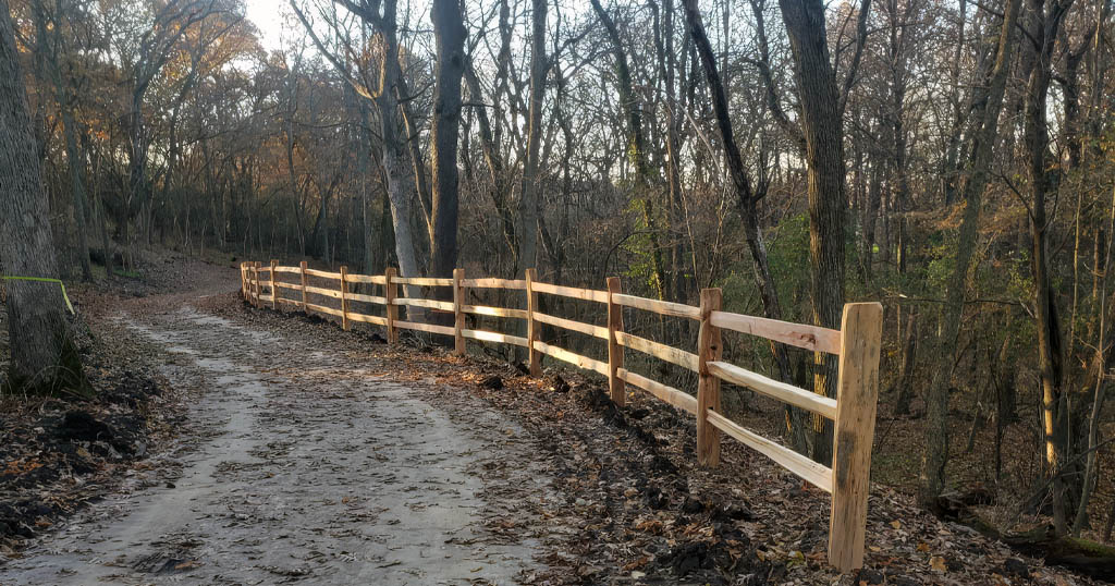 Wooden split-rail fence lining a leaf-covered trail through Sheiffer Park in northeast Janesville, Wisconsin.