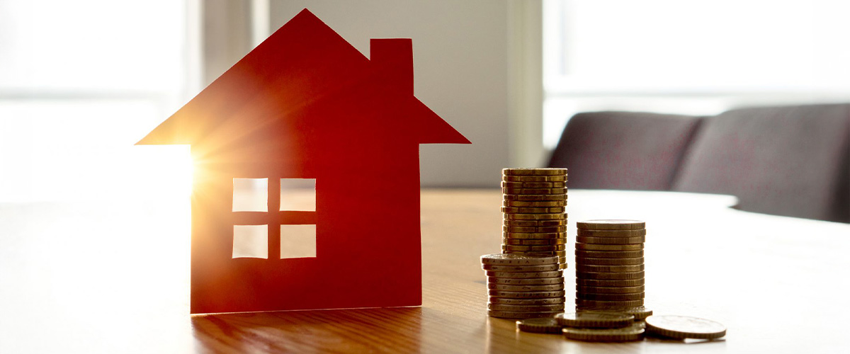 A red miniature house model sitting next to stacks of coins symbolizing the importance of setting a realistic asking price on a home listing.