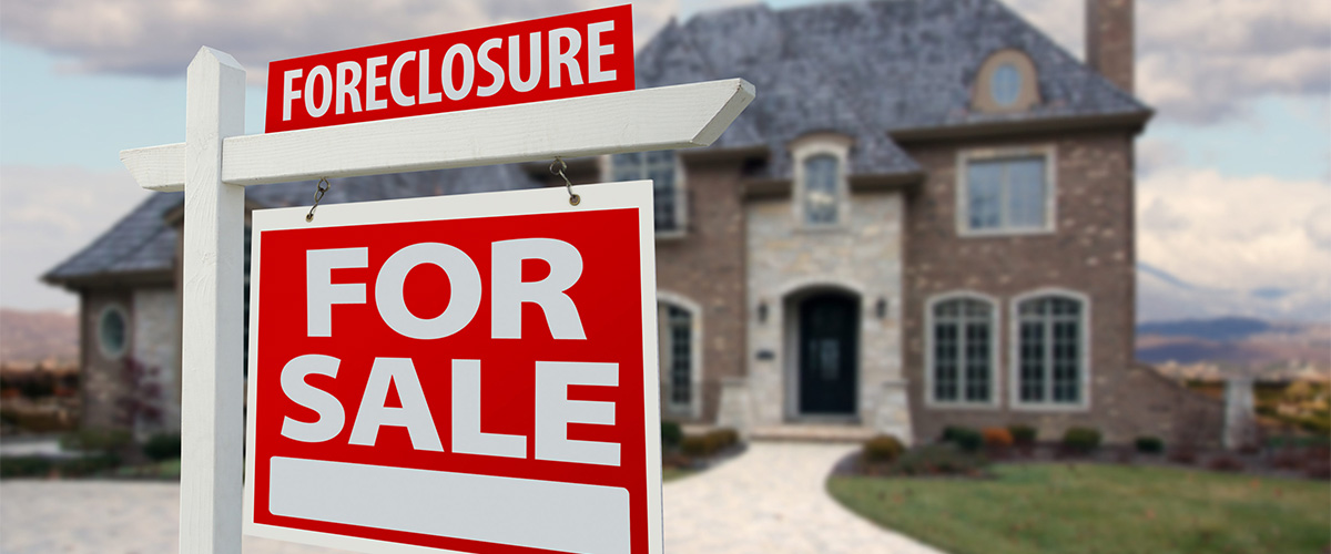 A red foreclosure and for sale sign standing in front of a suburban home symbolizing the rise in foreclosure filings in Q1 2025.