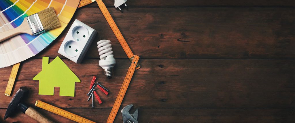 Construction tools and a house symbol against a wooden background symbolizing home improvement projects.