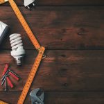 Construction tools and a house symbol against a wooden background symbolizing home improvement projects.
