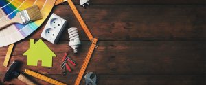 Construction tools and a house symbol against a wooden background symbolizing home improvement projects.