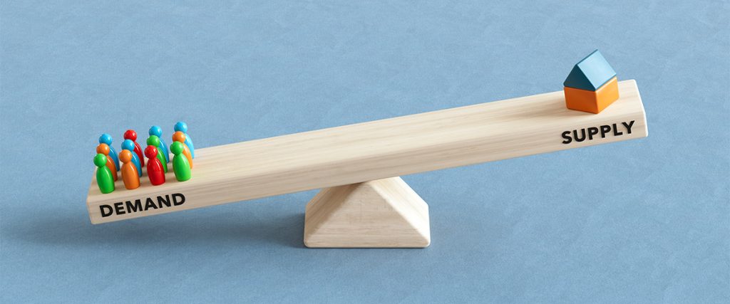 One side of a seesaw labeled "Demand" outweighs the other, labeled "Supply", symbolizing the balance of housing inventory.