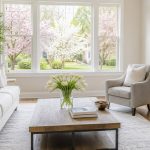 Bright staged living room with neutral decor, fresh flowers, natural light, and spring greenery outside.