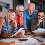Concerned family and advisor reviewing documents and a rising laptop graph regarding inflation and mortgage rates.