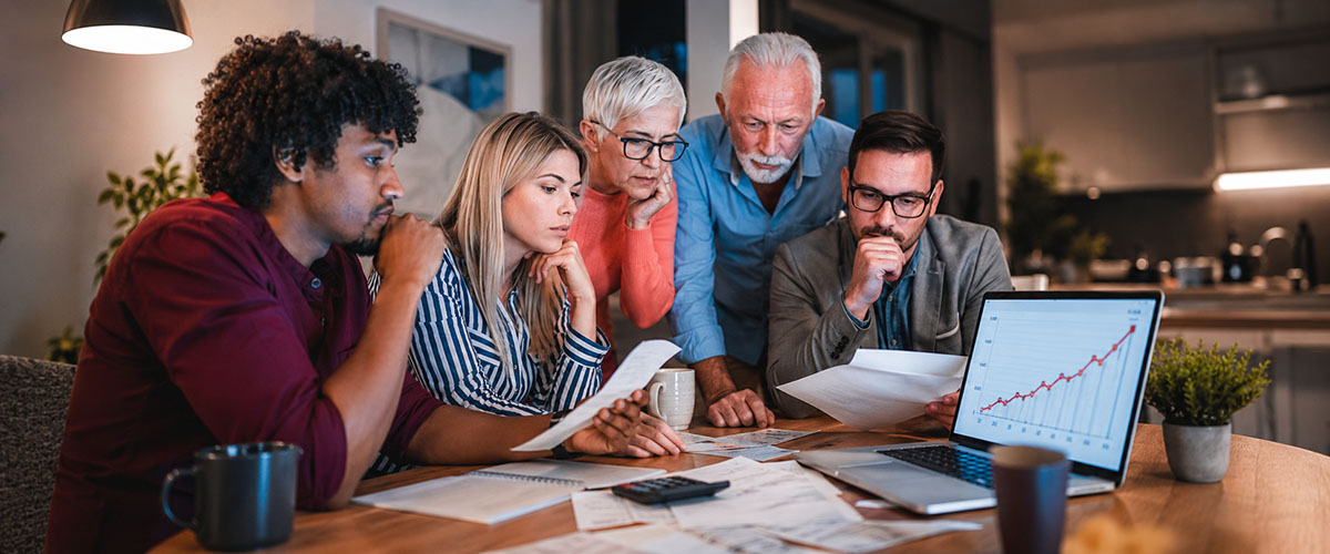 Concerned family and advisor reviewing documents and a rising laptop graph regarding inflation and mortgage rates.