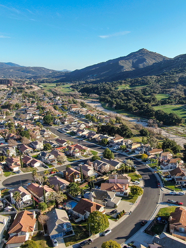 Suburban residential real estate in Temecula, California, showing houses with red tile roofs nestled near a local golf course and rolling hills.