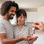 Real estate agent handing house keys to two smiling home buyers.