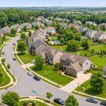 Aerial view of suburban single-family homes with green lawns and winding streets.