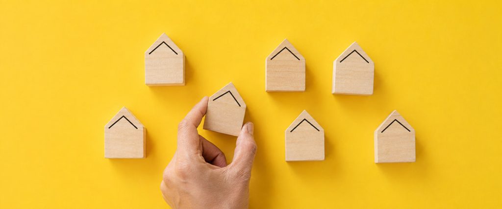 Hand placing a wooden house block among a group to represent available housing inventory.