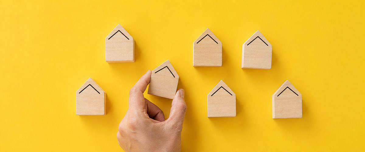 Hand placing a wooden house block among a group to represent available housing inventory.