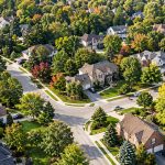 Homes and mature trees line winding streets in an aerial view of a neighborhood.