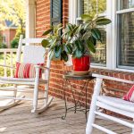 White rocking chairs and a potted plant sit on a wooden front porch.